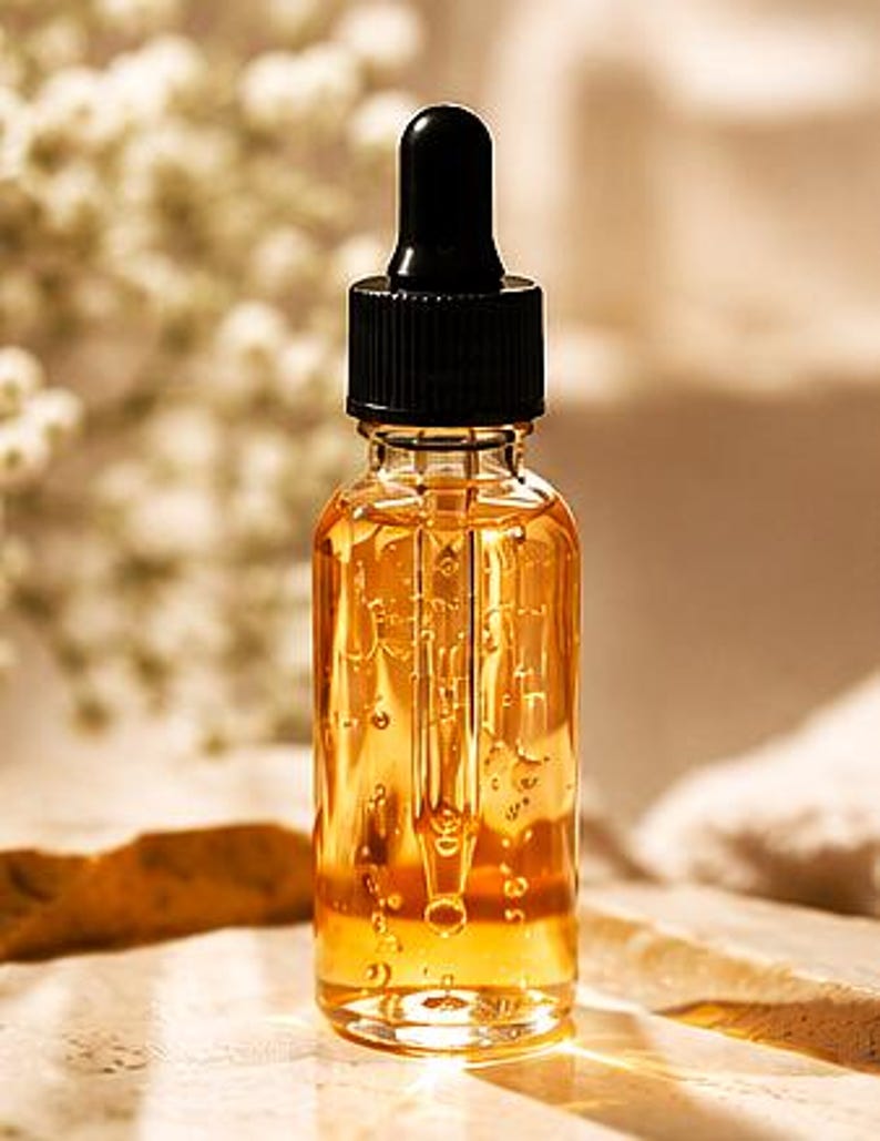 K&ouml;nnte beinhalten: Eine klare Glastropfflasche gef&uuml;llt mit einer gold-bernsteinfarbenen Fl&uuml;ssigkeit. Die Flasche verf&uuml;gt &uuml;ber einen schwarzen Schraubverschluss mit einer integrierten Glastropfpipette, die bis in die Mitte des Beh&auml;lters reicht. Die Fl&uuml;ssigkeit ist viskos.