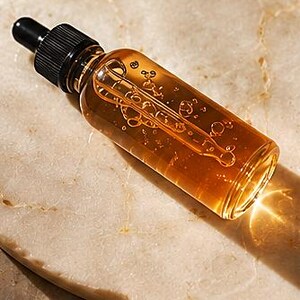 K&ouml;nnte beinhalten: Eine klare Glastropfflasche gef&uuml;llt mit einer gold-bernsteinfarbenen Fl&uuml;ssigkeit. Die Flasche hat einen schwarzen, gerippten Schraubverschluss mit einem schwarzen Gummiball. Im Inneren ist eine Glaspipette sichtbar, die in dem durchscheinenden &Ouml;l liegt.