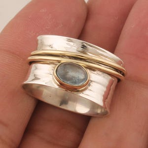 May include: A silver and gold spinning ring with a light blue gemstone. The ring is textured and has a hammered finish.