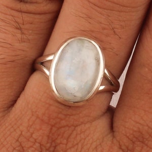 Puede incluir: Un anillo de plata con una gran piedra de luna ovalada engastada en un engaste de bisel. El anillo está en un dedo.