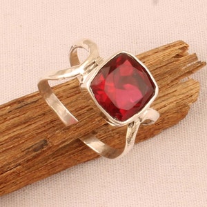 Könnte beinhalten: Ein silberner Ring mit einem roten Edelstein. Der Ring hat ein einzigartiges, verdrehtes Banddesign.