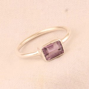 May include: A silver ring with a rectangular, light purple gemstone.