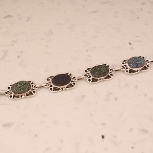 May include: A silver bracelet with four oval-shaped green and blue stones set in ornate silver frames. The bracelet has a toggle clasp.
