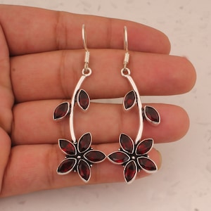 May include: A pair of silver dangle earrings with red gemstone flowers. The earrings feature a delicate branch design with multiple red gemstones.