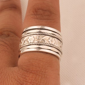 May include: A silver spinning ring with a floral design. The ring is made of multiple bands that spin freely.