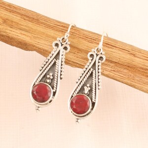 May include: A pair of silver dangle earrings with red gemstone accents. The earrings feature intricate filigree designs and a teardrop shape.
