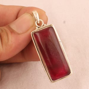Può includere: Un ciondolo d'argento con una pietra preziosa rossa rettangolare. Il ciondolo ha un design semplice ed è perfetto per aggiungere un tocco di colore a qualsiasi outfit.