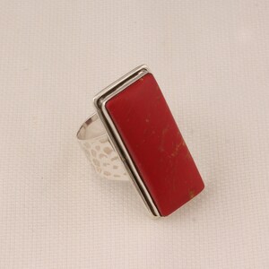May include: A silver ring with a rectangular red stone set in a silver frame. The ring band is textured.