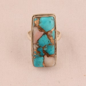 May include: A silver ring with a rectangular turquoise and pink stone set in a silver bezel.
