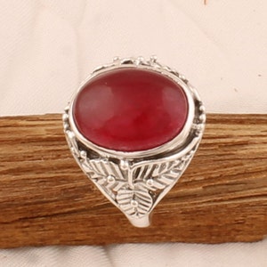 Può includere: Un anello d'argento con una pietra preziosa rossa incastonata in un design floreale.