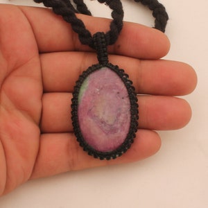 May include: A pink and green gemstone pendant with a black cord necklace. The pendant is oval shaped and has a macrame knot design.