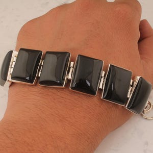 Könnte beinhalten: Ein Armband aus schwarzem Onyx mit silbernen Gliedern. Das Armband besteht aus rechteckigen schwarzen Onyxsteinen und silbernen Gliedern, die die Steine verbinden.