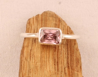 May include: A silver ring with a rectangular, light pink gemstone. The ring is set on a wooden surface with a light pink background. The gemstone is approximately 0.5 inches in length.