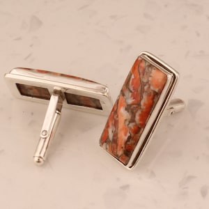 Puede incluir: Un par de gemelos de plata con una piedra rectangular roja y blanca.