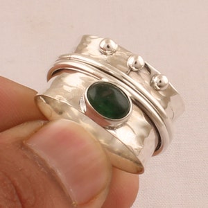 May include: A silver spinning ring with a green gemstone. The ring has a hammered texture and three small silver balls on the band.