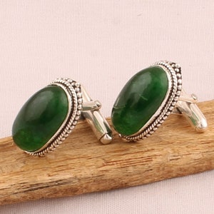 May include: A pair of silver cufflinks with green oval-shaped gemstones set in a beaded border.