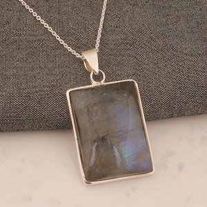 以下が含まれることがあります： 暗いグレーのラブラドライトの宝石が特徴の、長方形のペンダントが付いたシルバーチェーンネックレス。虹色の青と緑の輝きがあります。