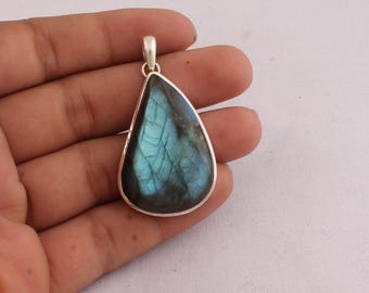 May include: A teardrop-shaped pendant with a silver bail. The pendant features a polished labradorite stone with iridescent blue and green hues. The stone is set in a silver bezel.