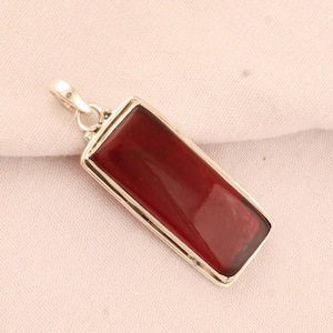 May include: A silver pendant with a rectangular red gemstone. The pendant has a simple design with a smooth, polished finish.