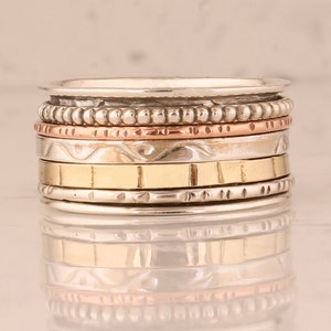 May include: A silver spinning ring with multiple bands, including a copper band, a gold band, and a band with a beaded design.