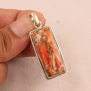 Op de afbeelding: Een zilveren hanger met een rechthoekige oranje en witte steen. De steen heeft een marmerpatroon.