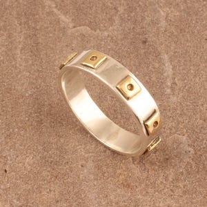 May include: A silver band ring with gold square accents. The ring has a smooth, polished finish.