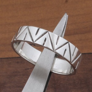 May include: A silver band ring with a geometric pattern of triangles and lines.
