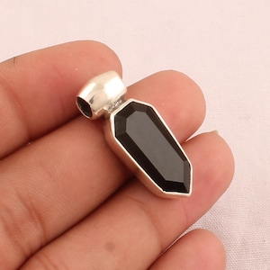 May include: A silver pendant featuring a black gemstone cut into an elongated, faceted shape. The pendant is displayed against a white backdrop.