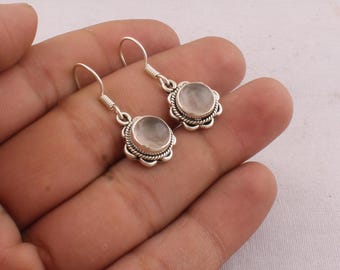 May include: A pair of silver earrings with a floral design. Each earring features a round, pale pink gemstone set within a decorative silver frame. The earrings have a hook closure.