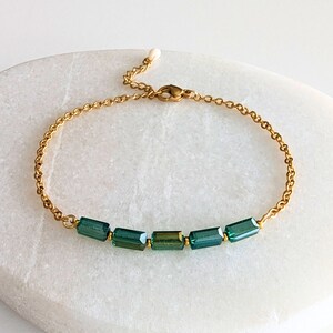 Peut inclure: Un bracelet en chaîne dorée avec une rangée de pierres rectangulaires vert foncé.