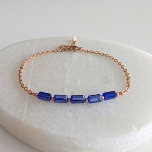 May include: A delicate rose gold chain bracelet with a row of dark blue rectangular glass beads.