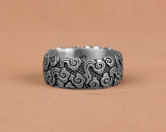 May include: A silver ring with a detailed design of swirling clouds. The ring is wide and has a textured surface.