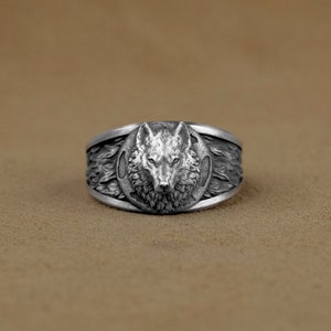 Peut inclure: Une bague en argent avec un motif de tête de loup. La tête du loup est entourée d'un cercle de fourrure.