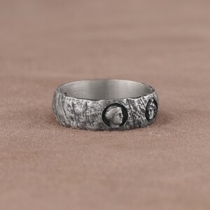 May include: A silver ring with a textured surface and three raised profile portraits.