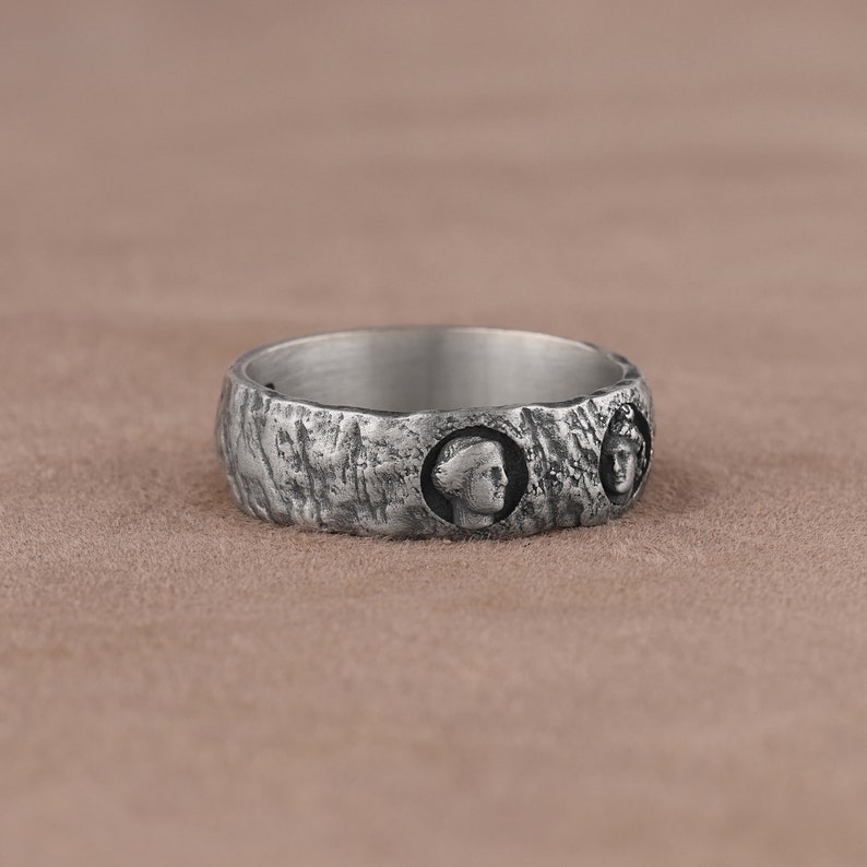 May include: A silver ring with a textured surface and three raised profile portraits.