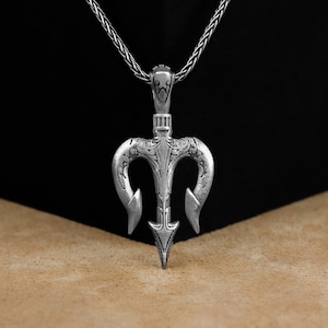 Puede incluir: Collar con colgante de plata con un diseño de tridente detallado. El colgante tiene una superficie texturizada y una punta puntiaguda.