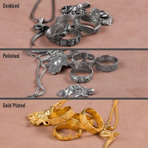 K&ouml;nnte beinhalten: Drei Reihen silberner Ringe und Halsketten mit verschiedenen Oberfl&auml;chen: oxidiert, poliert und vergoldet. Die Ringe haben komplizierte Designs, darunter eine Schlange, eine Hand und ein Fl&uuml;gel.