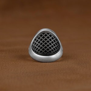 May include: A silver ring featuring a geometric, grid-like design. The ring is crafted from metal and has a smooth, polished finish.