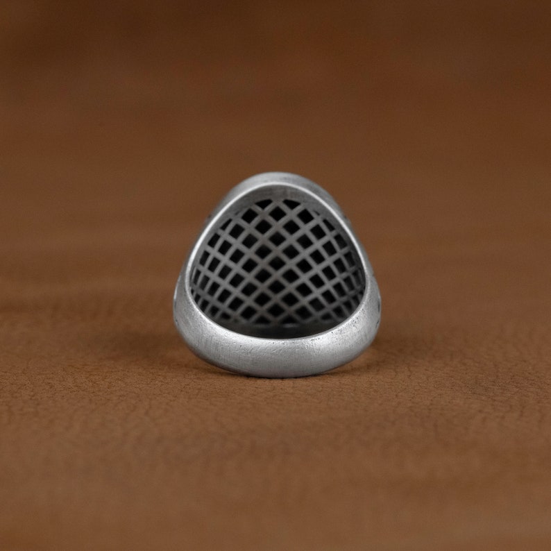 May include: A silver ring featuring a geometric, grid-like design. The ring is crafted from metal and has a smooth, polished finish.