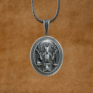 May include: A silver pendant necklace featuring a detailed design of a figure holding scales. The pendant is oval shaped and has a Greek key border.