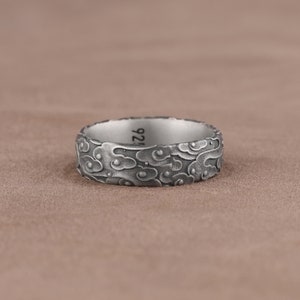 May include: A silver ring with a textured design of clouds. The inside of the band is engraved with the number "925".