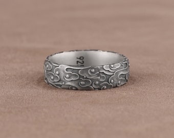 May include: A silver ring with a textured design of clouds. The inside of the band is engraved with the number "925".