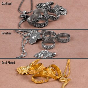 Puede incluir: Tres filas de anillos y collares de plata con diferentes acabados: oxidado, pulido y chapado en oro. Los anillos presentan dise&ntilde;os intrincados, incluyendo una serpiente, una mano y un ala.