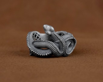 May include: A silver snake ring with a detailed, textured design. The snake is coiled and its head is raised.