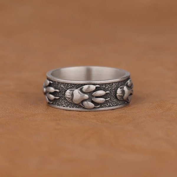 May include: A silver ring with a textured band featuring three raised paw prints.