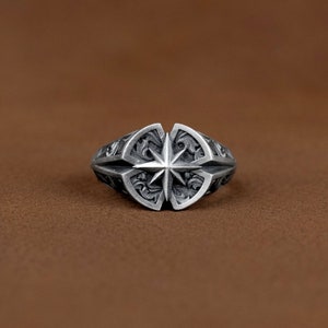 Könnte beinhalten: Ein silberner Ring mit einem detaillierten Design, das einen Stern in der Mitte und komplizierte florale Muster darum herum zeigt.