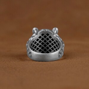 May include: Silver ring with a detailed design of a wolf's head. The ring has a black grid pattern inside the band.
