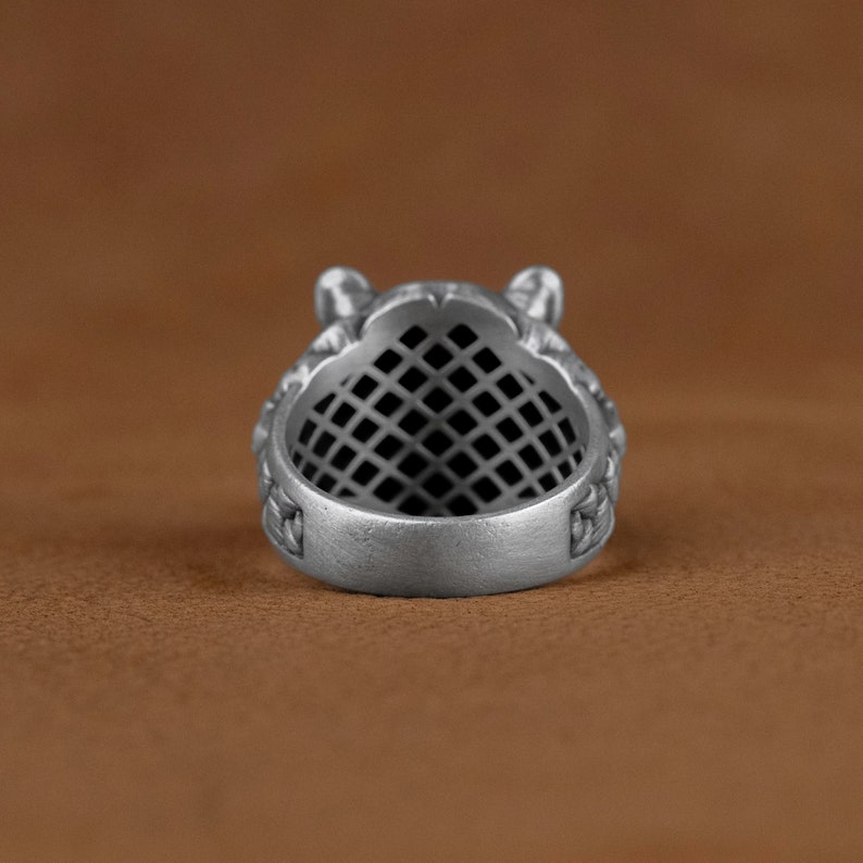 May include: Silver ring with a detailed design of a wolf's head. The ring has a black grid pattern inside the band.