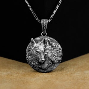 May include: A silver necklace with a round pendant featuring a detailed 3D design of two wolves facing each other.