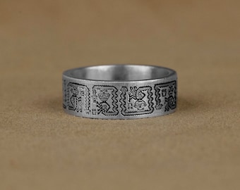 May include: A silver ring with a black geometric design. The design features repeating patterns of stylized figures.